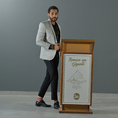 Hombre vestido con un blazer premium slim fit gris, pantalones oscuros y zapatos negros, de pie junto a un podio.