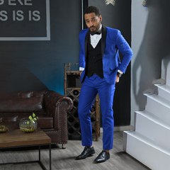 Hombre posando con traje azul brillante y corbata negra en un ambiente elegante.