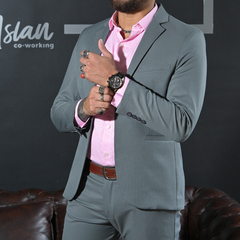 Hombre vestido con un traje gris y camisa rosa, mostrando anillos y un reloj en su muñeca.