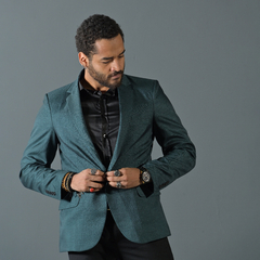 Hombre vistiendo un blazer slim fit verde inglés, ajustándose la chaqueta frente a un fondo gris.