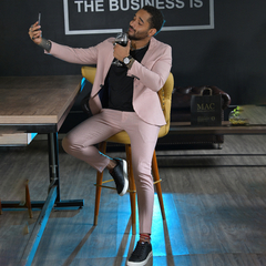 Hombre sentado en una silla alta, vestido con un traje rosa, tomando un selfie mientras disfruta de una bebida en un vaso.