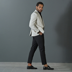 Hombre caminando con un blazer premium slim fit color tiza y pantalones oscuros, posando frente a un fondo gris.