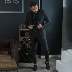 Hombre elegante vestido con un traje negro, ajustando su chaqueta mientras se encuentra en un ambiente moderno con muebles de cuero.