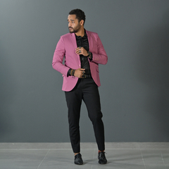 Hombre posando con un blazer premium slim fit de color rosa viejo, camisa negra y pantalón negro, en un fondo gris.