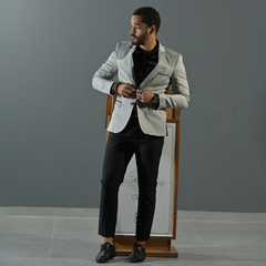 Hombre vistiendo un blazer premium slim fit gris, combinando con camisa negra y pantalones oscuros, ajustándose el blazer frente a un fondo gris.