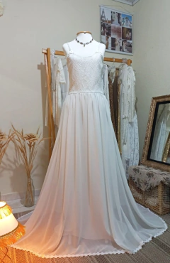 Vestido de noiva boho, com corpete de renda e saia fluida, exibido em um manequim em ambiente decorado.