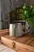 Taza de cerámica con diseño geométrico en tonos verdes y terracota, sobre una mesa de madera con un fondo de plantas y agua en la ventana.