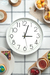 Reloj de pared blanco y negro sobre una mesa decorada con platos, frutas y tazas.