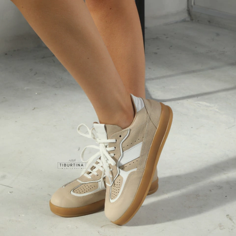 Zapatillas de mujer modelo Penny color natural con detalles blancos y suela marrón, puestas en pies femeninos sobre piso gris.