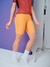 Mulher vestindo um kit de camisa e bretelle da Moove, na cor marrom e laranja, em um fundo roxo.