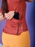 Modelo feminina vestindo uma camisa de cor vermelho escuro, colocando um celular em um bolso lateral.