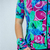 Detalhe de uma camisa feminina de ciclismo com estampa colorida e vibrante, combinando tons de rosa, verde e azul, acompanhada de um manguito correspondente.