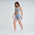 Mulher usando shorts feminino cinza mescla da marca Marcio May Sports, posando de lado com um fundo branco.