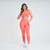 Modelo usando calça legging feminina laranja da Marcio May Sports, com top combinando e tênis brancos.