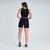 Mulher vista de costas usando shorts femininos pretos da linha Marcio May Sports Romilla, com um top preto, em um ambiente neutro.