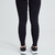 Calça legging feminina preta Marcio May, vista traseira, com detalhes texturizados e combinada com tênis esportivos.