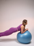 Mulher fazendo exercício em bola de pilates, vestindo calça legging feminina roxa da Marcio May Sports.