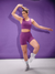 Modelo usando shorts femininos roxos da marca Marcio May, com um fundo roxo, demonstrando uma pose atlética.