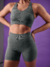 Top feminino esportivo verde mescla, modelo com alças largas e decote em V, utilizado por uma mulher em fundo roxo.