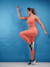 Mulher usando calça legging feminina laranja da marca Marcio May Sports, fazendo exercício em fundo azul.