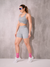 Modelo feminina usando shorts cinza mescla e top de fitness, com meias rosa e tênis brancos, posando em fundo neutro.