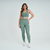 Modelo vestindo um conjunto de top e calça legging verde mescla da Marcio May Sports.