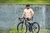 Homem sentado em uma bicicleta, vestindo uma camisa de ciclismo cor pêssego, com detalhes em rosa.