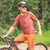 Homem usando camisa de ciclismo Márcio May Aero Caju, com detalhes em vermelho e laranja, posando ao lado de uma bicicleta em um ambiente natural.