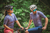 Casal em ambiente natural usando camisas de ciclismo Marcio May Highline Gravity, com detalhes em azul e padrões modernos, ambos com capacetes e óculos de sol.