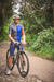 Homem em uma estrada de terra usando um kit de ciclismo marinho com bretelle, segurando uma bicicleta.