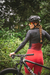 Macaquinho ciclismo feminino com manga longa, modelo Marcio May Moove, na cor vermelha, usado por uma ciclista em meio à natureza.