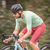 Atleta pedalando em alta velocidade, vestindo uma camisa de ciclismo verde e bermuda vermelha da marca Márcio May.