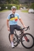 Homem sentado em uma bicicleta, usando camisa de ciclismo azul com detalhes nas cores da bandeira da Bélgica e calças esportivas pretas.