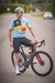Homem em uma bicicleta usando a camisa Highline País do Ciclismo da Bélgica, com cores vibrantes e detalhes em preto.