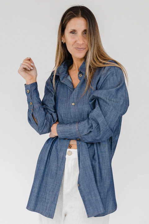 Mujer luciendo la camisa Siena de denim azul con corte irregular en la espalda y solapa que cubre los botones frontales