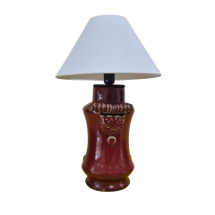 ista frontal da base para abajur em cerâmica vermelho escuro/bordô (SKU CJ0036A), com adornos em relevo no centro. A imagem exibe uma cúpula branca cônica que é apenas ilustrativa e não acompanha o produto.