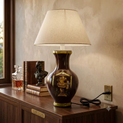 Ambiente aconchegante com abajur de cerâmica decorativo (SKU CJ0283A), com base marrom profunda pintada à mão com design clássico de urna e grinaldas verdes, sobre um aparador de madeira ao lado de livros antigos e um busto. A cúpula mostrada é meramente 