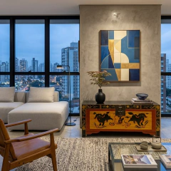 "Uma sofisticada sala de estar em um apartamento contemporâneo no Brasil, com vista para a cidade ao anoitecer através de grandes janelas. O centro da cena é um autêntico baú oriental artesanal (preto com painéis vermelhos e amarelos pintados à mão com fi
