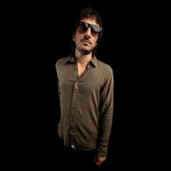 Hombre con camisa lisa de lino verde manga larga y gafas de sol oscuras sobre fondo negro