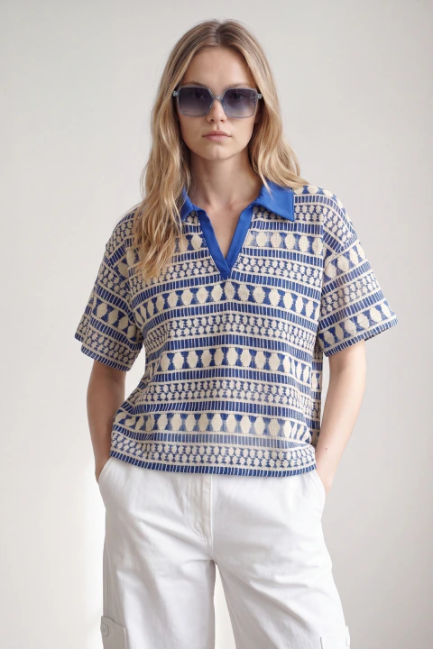 Remera Doradillo tejida con escote en V y cuello camisero azul, modelo usando anteojos de sol y pantalón blanco.