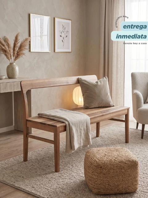 Banco Estanislao de madera clara con respaldo, cojín gris y manta beige en un living decorado con alfombra, cuadro y luz ambiental