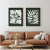 Composição de dois quadros decorativos com arte botânica em tons escuros, exibindo flores e folhas estilizadas em branco sobre fundo verde escuro, pendurados em parede acima de sofá de couro marrom