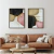 Composição de dois quadros decorativos abstratos em tons de preto, rosado, dourado e bege com moldura preta, acima de sofá de couro marrom em sala de estar moderna