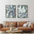 Dois quadros decorativos com folhagens em tons de cinza e branco, emoldurados, pendurados acima de um sofá de couro marrom.