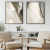 Dois quadros decorativos com arte abstrata em tons neutros, pendurados em uma parede branca, ao lado de poltronas em um ambiente moderno.