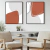 Dois quadros decorativos com formas abstratas em tons de coral e cinza, emoldurados em preto, exibidos em uma sala aconchegante.