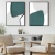 Dois quadros decorativos com formas geométricas em tons de verde e cinza, emoldurados em preto, exibidos em uma sala com poltronas de madeira.