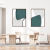 Dois quadros decorativos com formas abstratas em tons de verde e cinza, pendurados em uma parede branca, com uma mesa de madeira e cadeiras ao fundo.