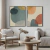 Dois quadros decorativos com arte abstrata em cores neutras, com formas orgânicas e suaves, pendurados em uma parede branca acima de uma sala de estar minimalista.