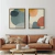 Dois quadros decorativos com fundos de cores neutras e formas abstratas, pendurados em uma parede branca acima de um sofá de couro marrom claro, decorado com almofadas em tons suaves.